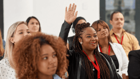 A woman raises her hand among a group of attendees at a conference.